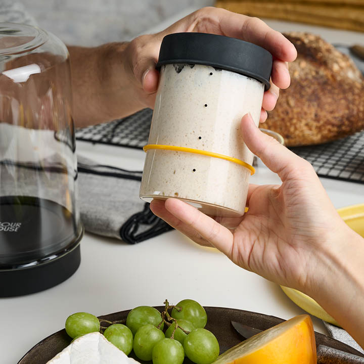 Hand holding Sourhouse glass sourdough starter jar with silicone lid and active starter inside