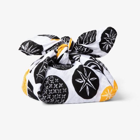 A loaf of bread wrapped in a black and gold patterned cloth, tied with a knot.